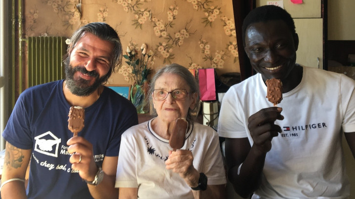 Deux bénévoles et une femme agée mangent une galce en souriant au photographe