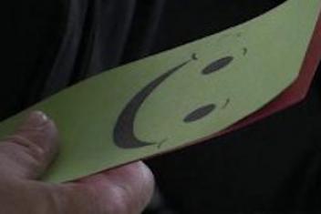 Main tenant un papier jaune sur lequel un smiley souriant est imprimé