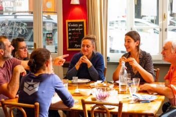 Groupe de convives souriant discutant autour d'un repas à la table de la Petite cantine de Lyon Perrache.