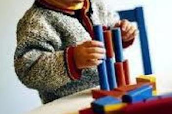 Un petit garçon joue avec des jouets en bois. Il est en train de construire une tour avec les éléments du jeu qui sont bleus et rouges. 