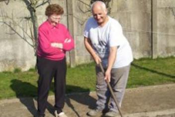 Deux personnes retraitées sont en train de jardiner. L'homme a un râteau à la main, et la femme regarde, à ses côtés