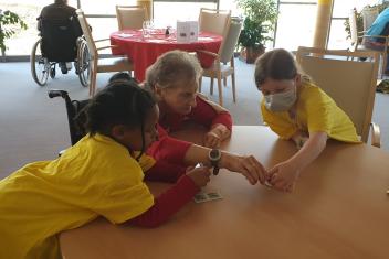 Une femme âgée assises joue à table avec deux enfants.