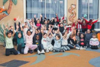 Groupe d'enfants alignés dans une cour d'école face à l'appareil photo. Bras levés.